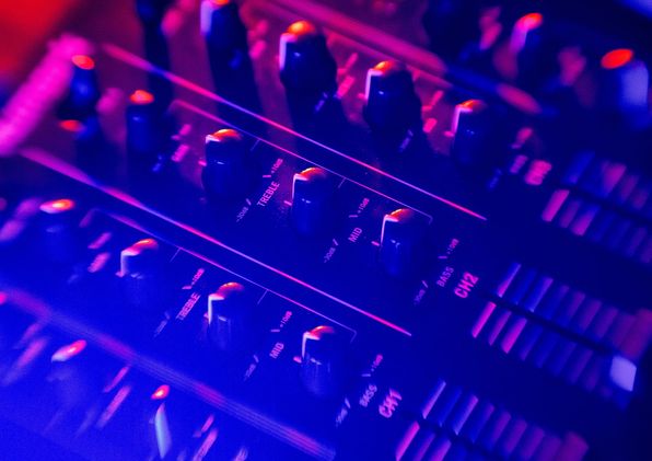 Close-up of a mixing console's knobs and faders lit in blue and magenta