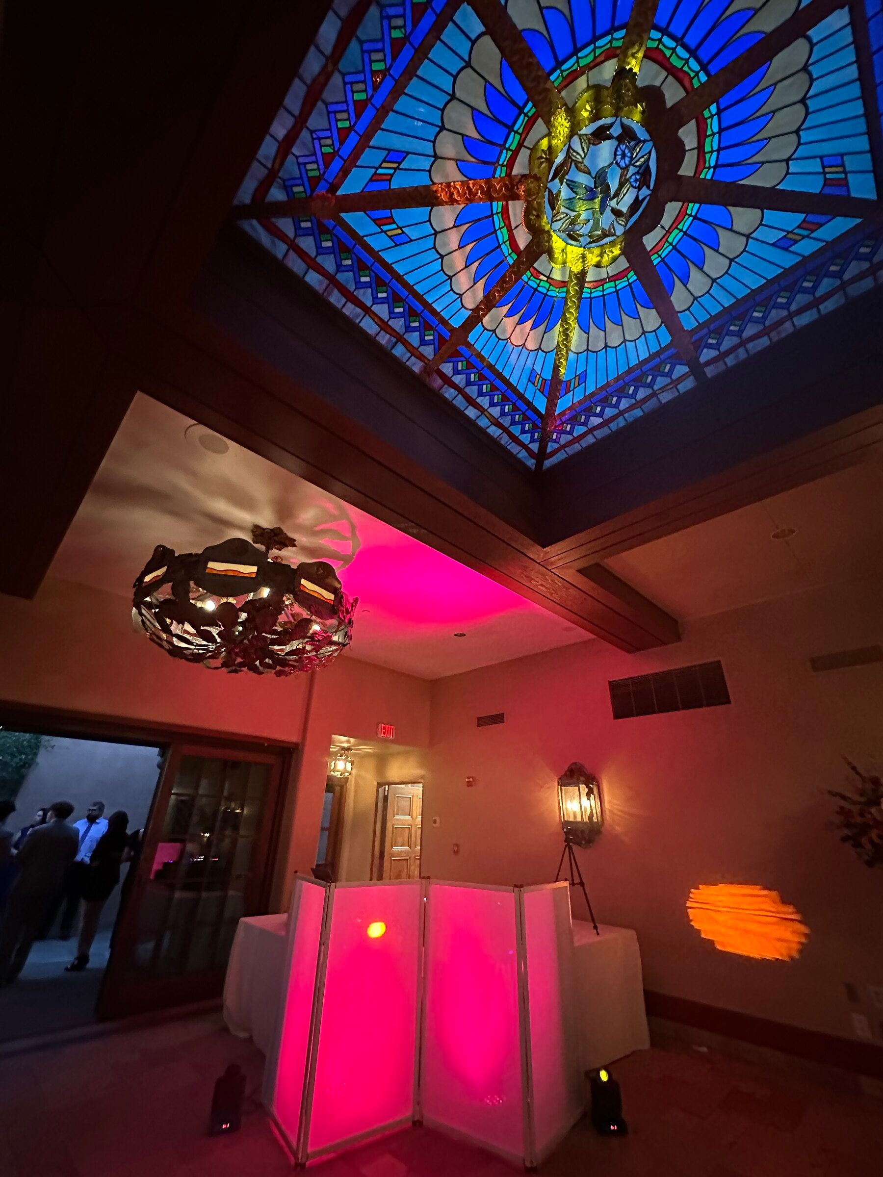 Pink-lit DJ booth under a stained glass skylight in a darkened hall