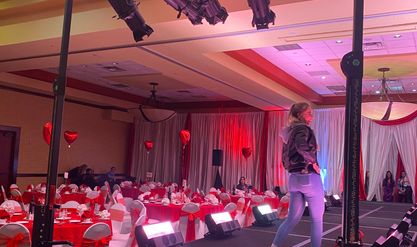 A model walking a banquet hall runway lit in pink and red by truss-mounted stage lights