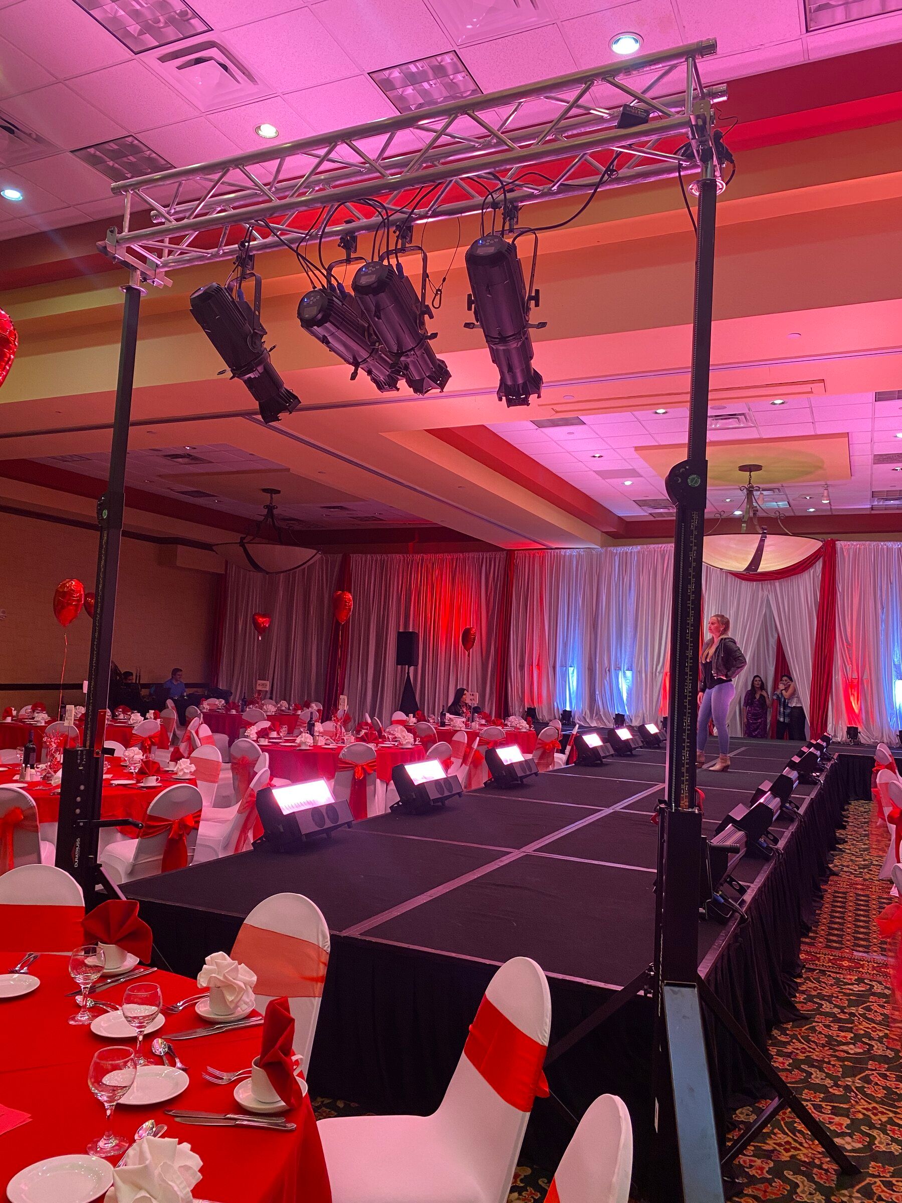 Truss of moving lights over a banquet hall runway, with red-draped tables on both sides