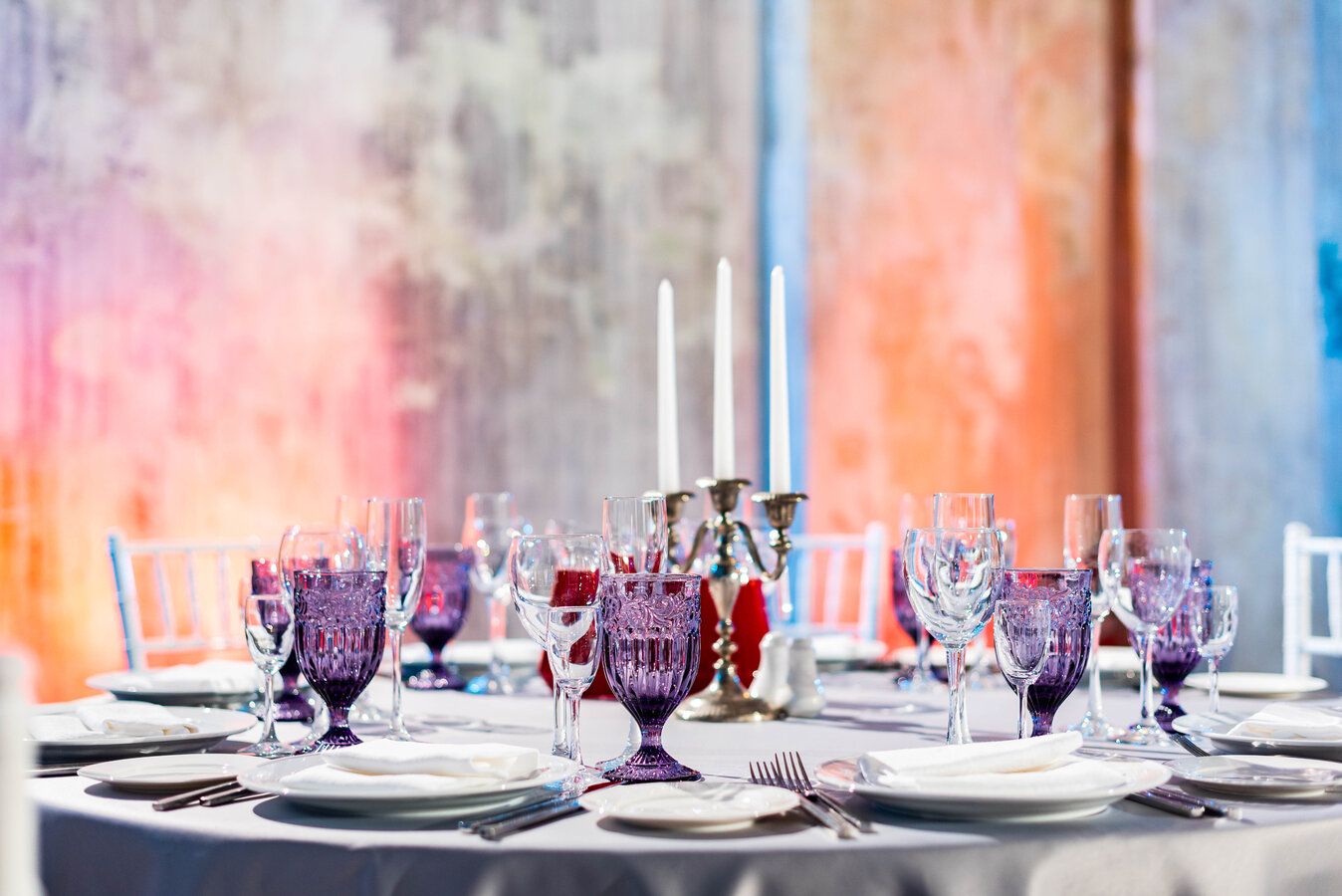 Formal round table set with a silver candelabra and purple goblets against walls washed in colored light