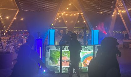 Guests dancing under blue light inside a geodesic dome, with photos projected across the DJ booth