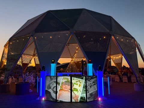 Geodesic dome venue at dusk with a lit DJ booth and blue light towers set up outside