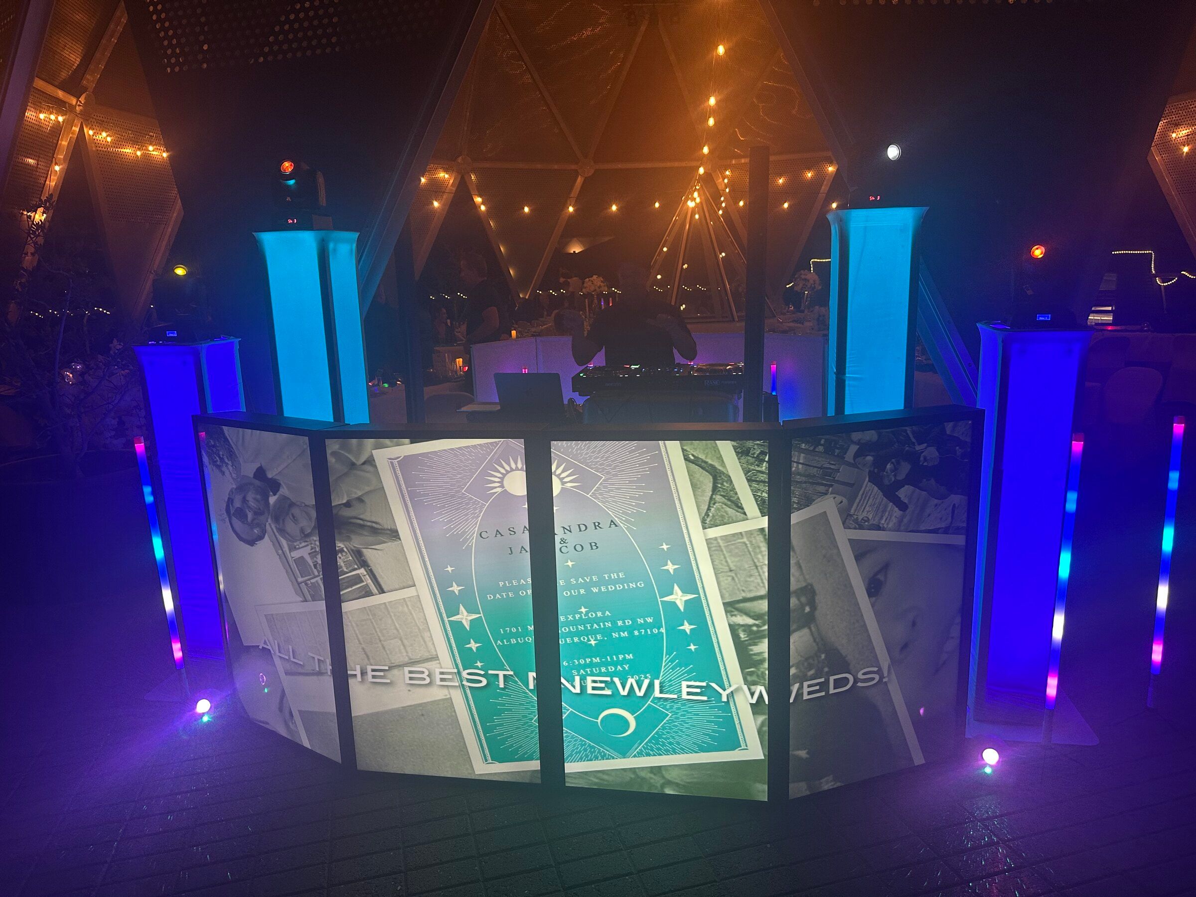 DJ booth façade lit with a projected save-the-date graphic, flanked by glowing blue light towers