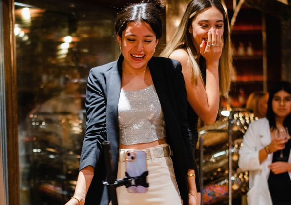 Friends raising champagne glasses in front of a wall of bulb lights as confetti falls