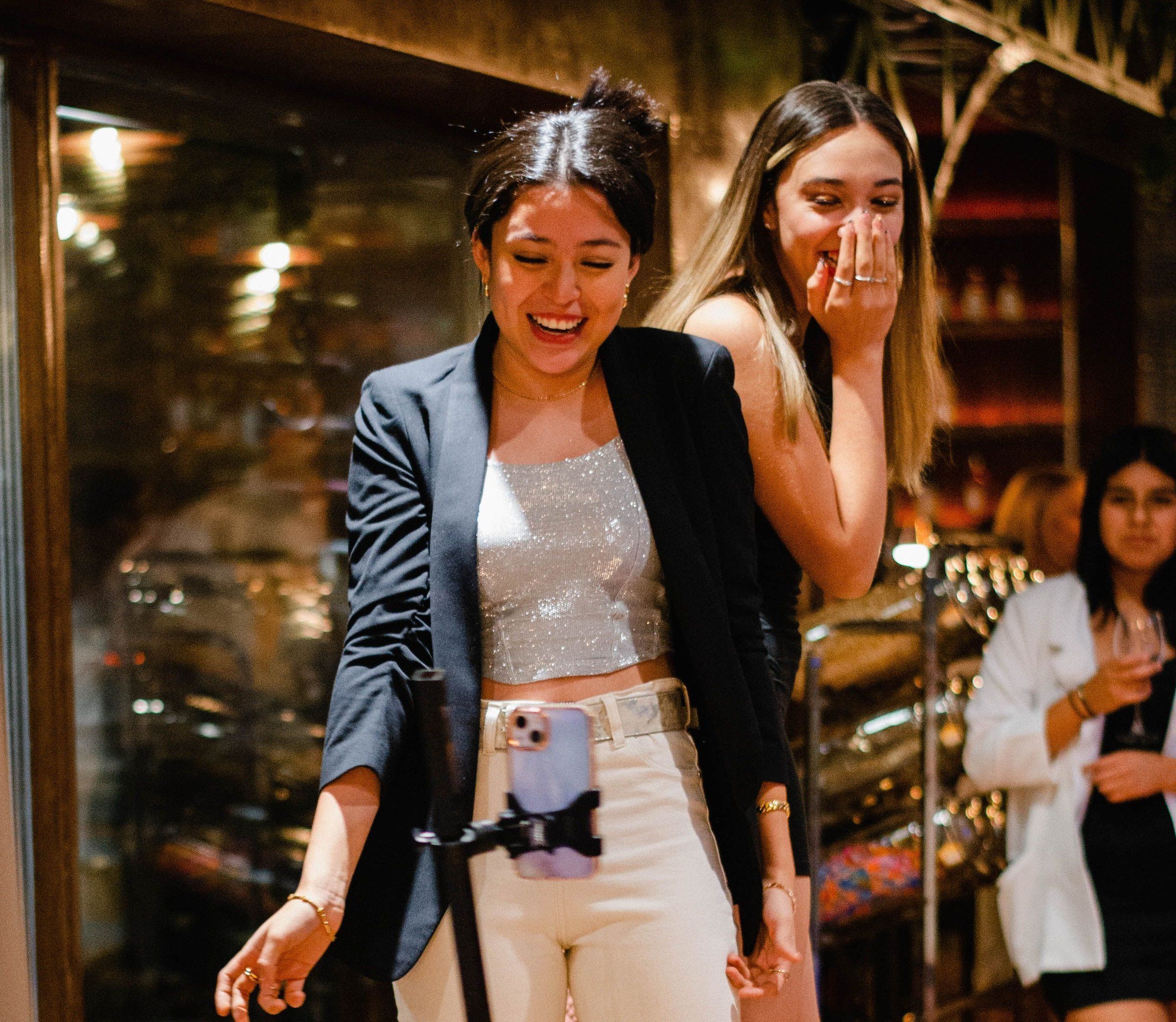 Two friends laugh on a 360 photo booth platform as the camera arm spins around them at an evening party