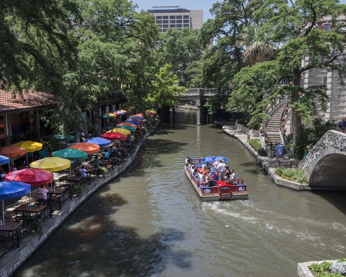 Tour barge passing colorful cafe umbrellas on the San Antonio River Walk