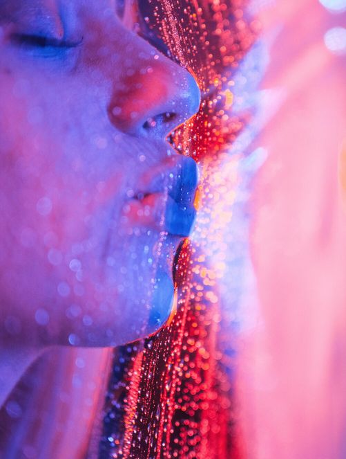 Close-up of a face lit in pink and blue under glittering event lights